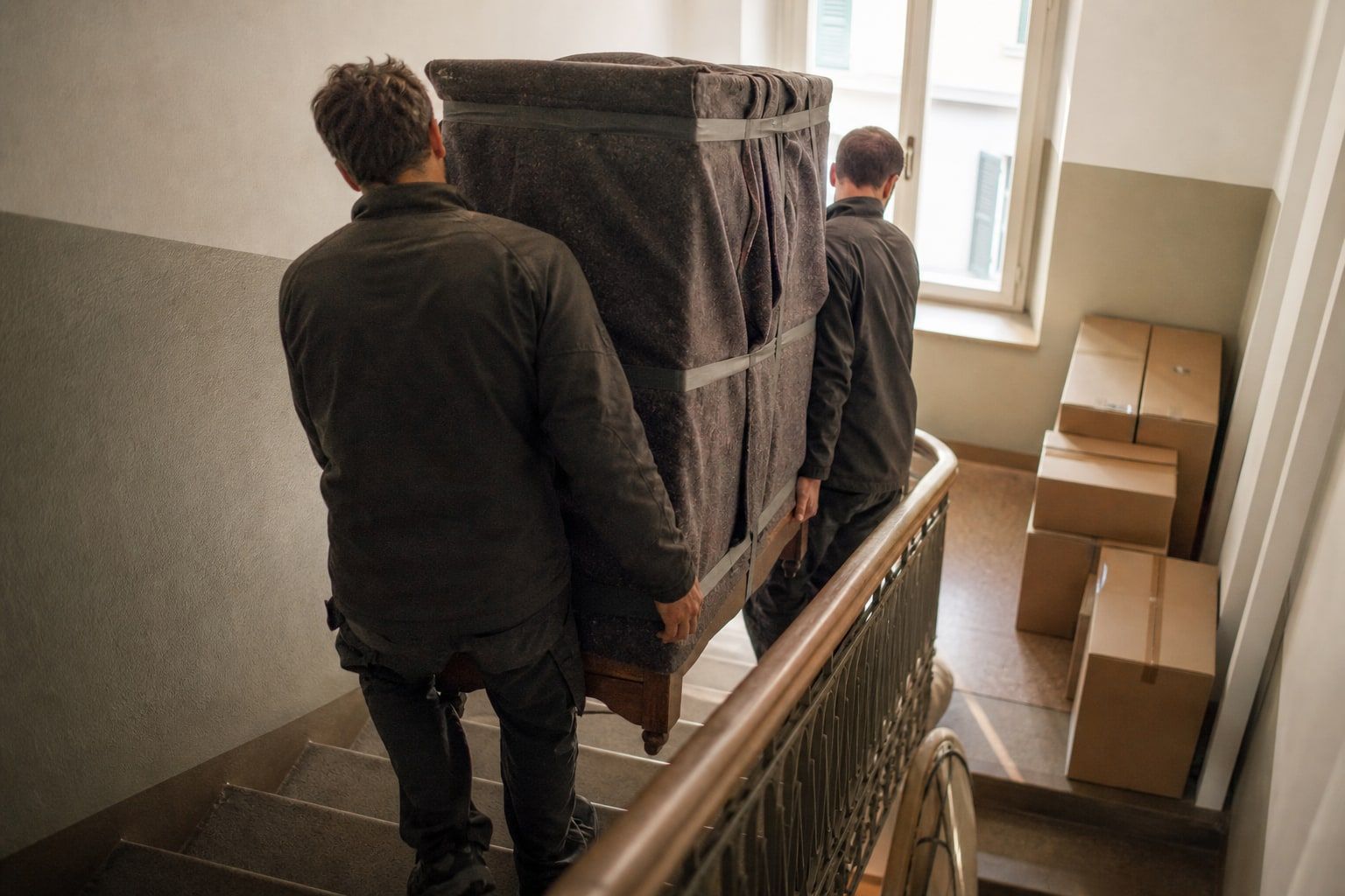 Zwei Personen tragen einen verpackten Schrank durch ein Treppenhaus